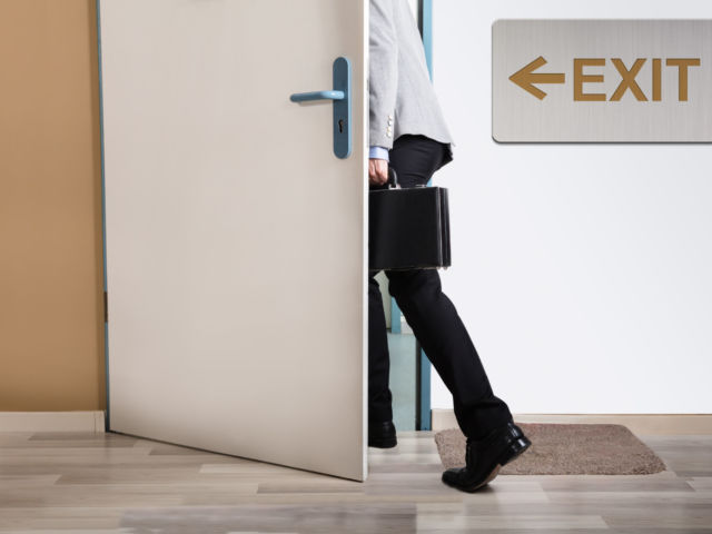 Businessperson Walking Out With Exit Sign On Wall